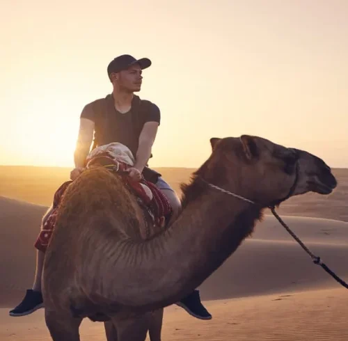 Tourist riding a camel across the golden desert dunes in Dubai